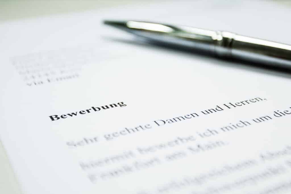 Close-up of a document with the German word "Bewerbung" and a silver pen resting on it