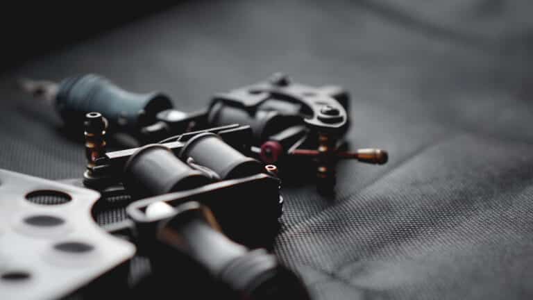 Close-up of tattoo machine parts and grips scattered on a dark textured surface as they lay ready for use in tattooing